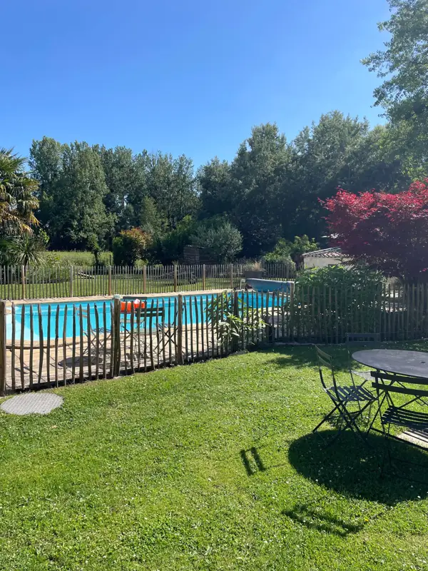 La piscine vue depuis la pelouse, avec une table de jardin au premier plan.